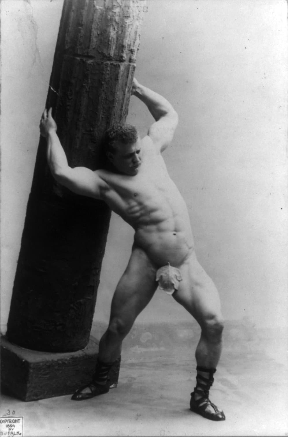 Sandow leaning on a pillar in a Samson pose
