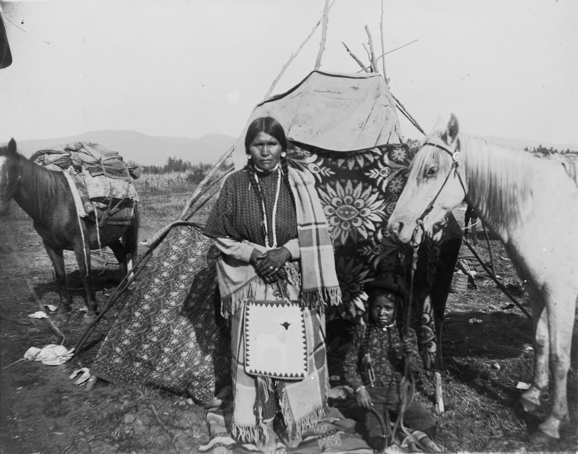 Little Woman Mountain and son Looking-away-off in front of tipi with two horses